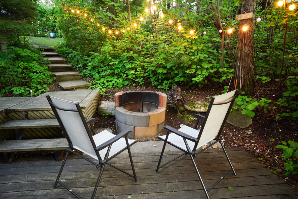A beautiful shot of white chairs in front of an outdoor fireplace in a garden with ferry lights