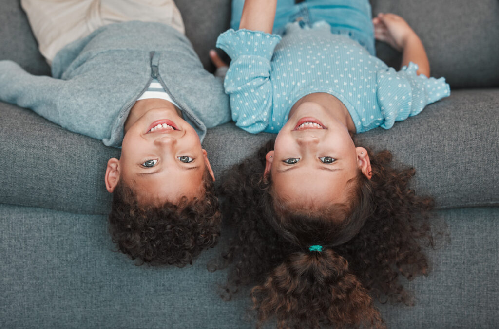 Portrait, upside down and siblings on couch, kids and bonding together with game in living room. Face, children and sister with brother on sofa, playful and home with activity, cheerful and happiness.