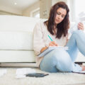 Woman working out her finances at home sitting on the floor with notepad and calculator