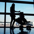 Silhouette of a mum with a pram against a full size window at an airport with view of runway and a plane