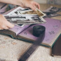 Ladies hands holding old photo album with a pile of old photos and a roll of film