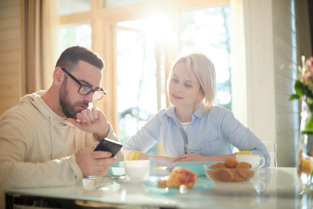 A couple sitting in the kitchen having breakfast and looking at a mobile phone