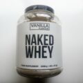 A large tub of Naked Whey protein powder in Vanilla flavour on a white desk