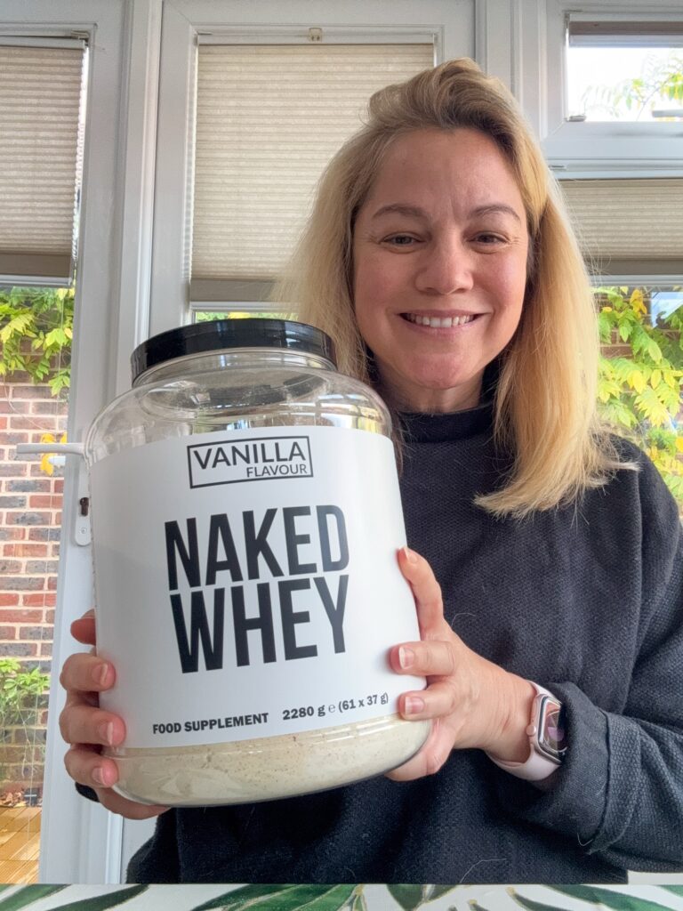 Healthy looking woman in her forties holding a big tub of Naked Whey protein powder