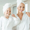 Mum and daughter brushing their lovely white teeth together looking in a mirror in white dressing gown and towel turbines
