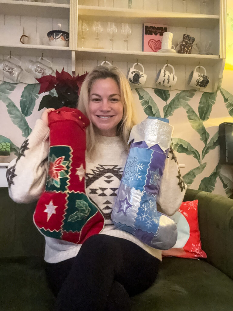 Lady with two Christmas stockings sitting in her kitchen on a green sofa
