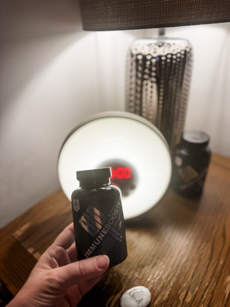 Lady's handholding immunity support vitamins by her bedside table with her alarm clock behind indicating it's morning