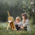 Two young girls sitting by an easel in nature