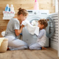 Mum and young child in their kitchen by washing machine smelling laundry