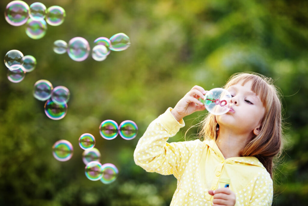 Young girl in yellow top blowing bubbles