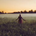 Solitary woman in a field with er arms outstretch facing the sunrise