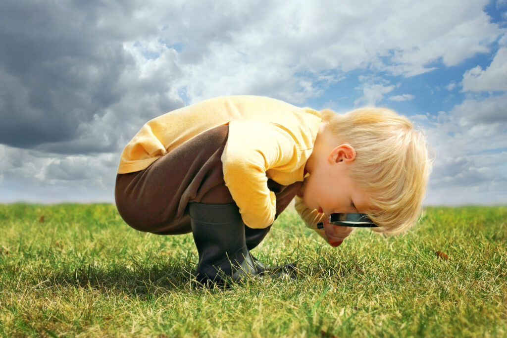 Toddler boy looking through a magnifying glass at grass in the garden