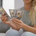Lady with dollar notes sitting on the sofa looking at her money