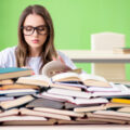 Young female student preparing for exams with many books on the desk and a green background