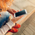 Woman sitting down and looking at her mobile with her long red hair hanging loose