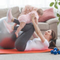 Young pretty mother working out with her little child at home