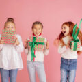 Three girls jumping for joy each with a beautifully wrapped present - pink background