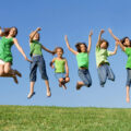 Happy kids in green summer camp tops jumping in the air for