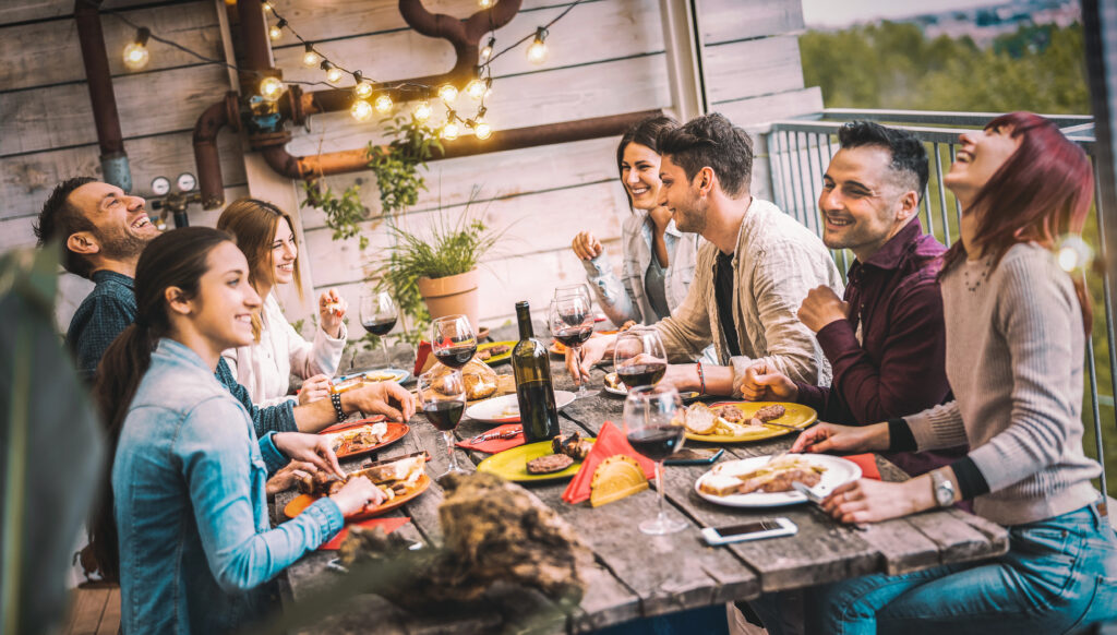 A group of people sat outside on a table chatting, eating dinner and having fun together