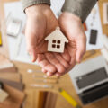A hand holding a cut out house with DIY equipment spread out on the table underneath
