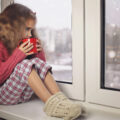 Young girl by the window looking out at the cold in her cosy pjs and drinking a warm hot chocolate grateful for the double glazing to help keep warm.