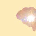 Hand holding up a model of a brain with a jigsaw piece in the missle and light shining through to represent focus and mental clarity